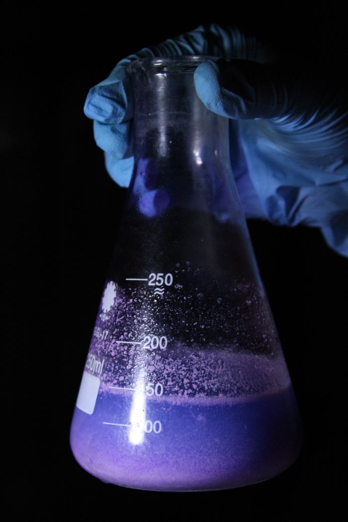 About Purple solution reacts inside Erlenmeyer flask, highlighted against dark background.